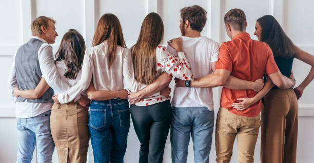 grupo de jóvenes abrazando juntos vista trasera - enfold fotografías e imágenes de stock