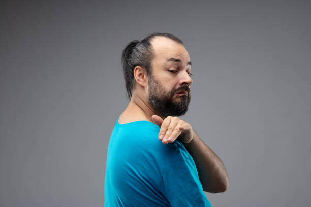 Man showing contemptuous gesture over his shoulder Bearded man in blue t-shirt showing contemptuous gesture with a hand over his shoulder, as if dusting off, and grimace of disgust on his face. Side portrait against grey background derogatory stock pictures, royalty-free photos & images