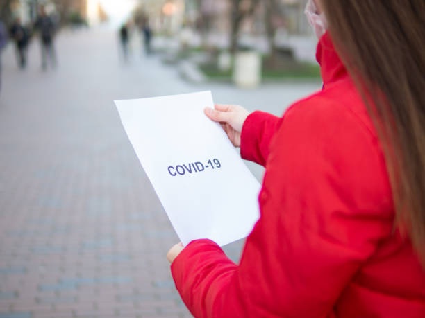 istock Woman standing outdoors holding a printed on white paper with covid-19 text printed on it. 1215592852
