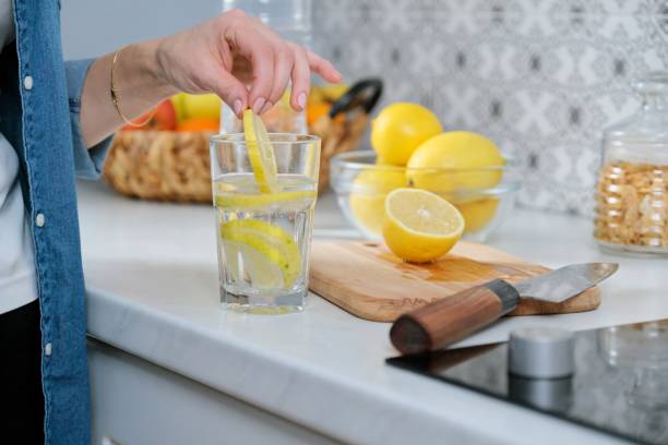 main femelle avec la tranche de citron dans la cuisine, avec l’eau pétillante avec le citron - waterlemon photos et images de collection