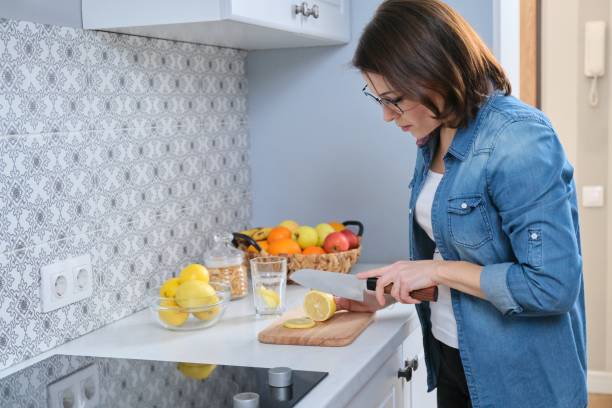 istock Woman cutting lemon with knife on cutting board in the kitchen 1215593786