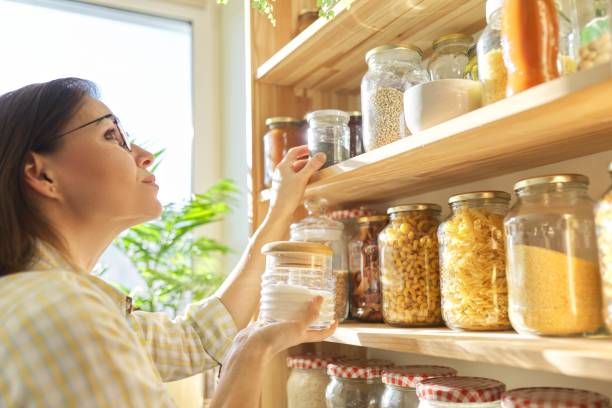 Food storage in pantry, woman holding jar of sugar in hand. Food storage in pantry, woman holding jar of sugar in hand. Pantry interior, wooden shelf with food cans and kitchen utensils rice food staple stock pictures, royalty-free photos & images