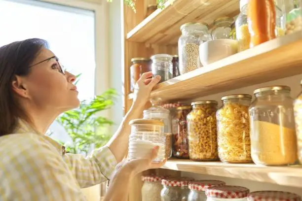 Photo of Food storage in pantry, woman holding jar of sugar in hand.