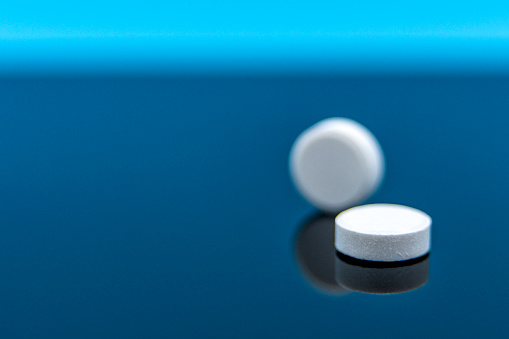 A pair of tablets of acetaminophen arranged in studio upon a reflective surface against a blue background with copy space.