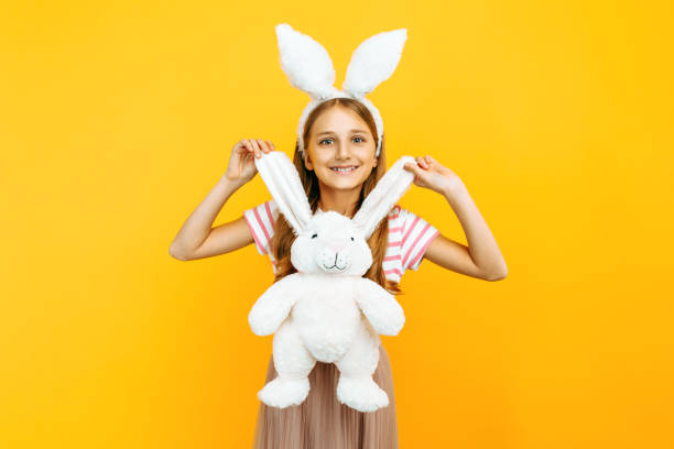 istock A happy girl on a head with rabbit ears holds a plush Easter Bunny on a yellow background 1215599057