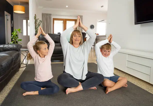 COVID-19 Shutdown. Caucasian family doing yoga at home in quarantine. Mother, daughter and son doing meditation during lockdown. Health, exercise stay at home and self-care for coronavirus isolation.