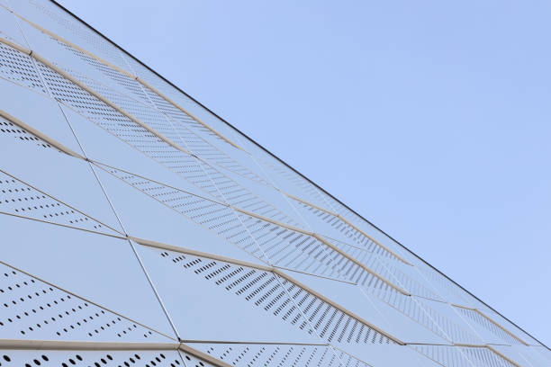 istock Wide angle view of metal wall with triangular pattern and round openings against blue sky 1215601220