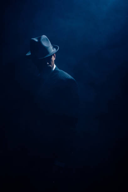 istock Silhouette of mafioso in suit and felt hat on dark blue background 1215603108