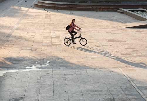 A young mexican woman with a backpack riding a bike in the city and going to work in the morning.