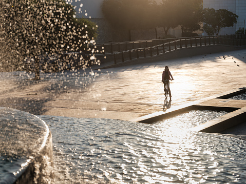 A woman riding her bike in the city near a fountain.