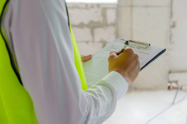 constructor de capataz, ingeniero o inspector en el chaleco de seguridad verde verificación e inspección con portapapeles en el interior del edificio de la construcción, inspección, contratista y concepto de ingeniería - inspector fotografías e imágenes de stock