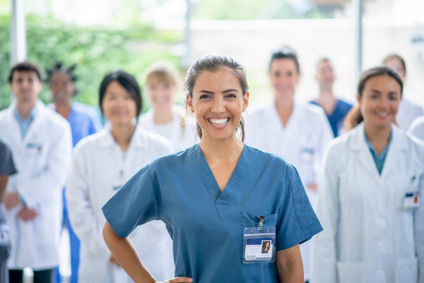 Group of Medical Professionals stock photo A multi-ethnic group of health professionals pose together for a photo.  They are lead by a strong mixed-race female in blue scrubs.  The medical personnel behind her are out of focus and are all dressed in white lab coats or scrubs. israeli ethnicity stock pictures, royalty-free photos & images