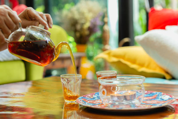 istock Woman pouring tea into a cup from tea pot on wooden table. 1215620148