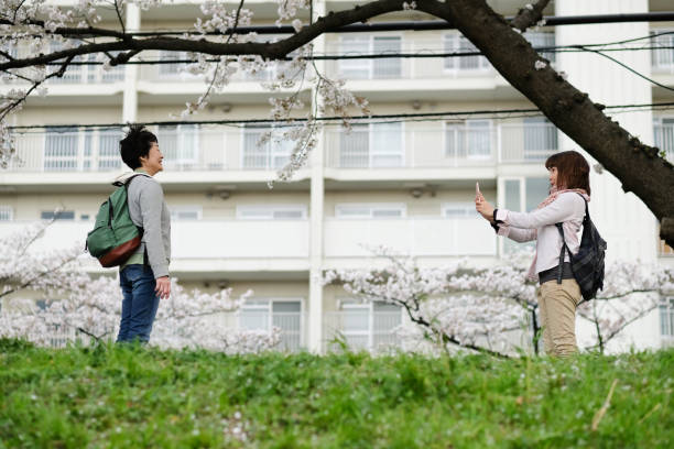 Mid-adult daughter taking picture of senior mother under cherry trees