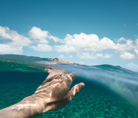 Man swimming in crystal clear water. Personal perspective from the water.