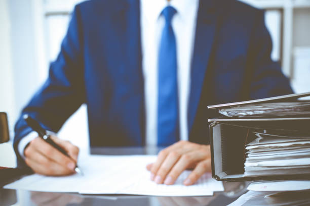 istock Binders with papers waiting to be processed with businessman or bookkeeper back in blur. Accounting planning budget. Audit, insurance and business concept 1215635752