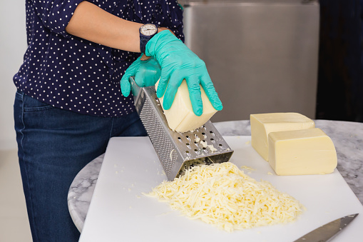 Woman with green gloves grating cheese on kitchen table