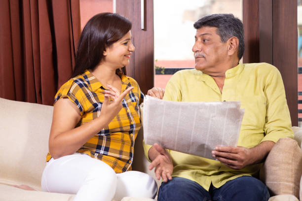 Father and daughter in law reading newspaper and discussing early morning Father discussing newspaper headlines with daughter at home in morning father in law stock pictures, royalty-free photos & images