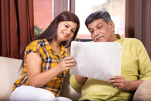 Father discussing newspaper headlines with daughter at home in morning