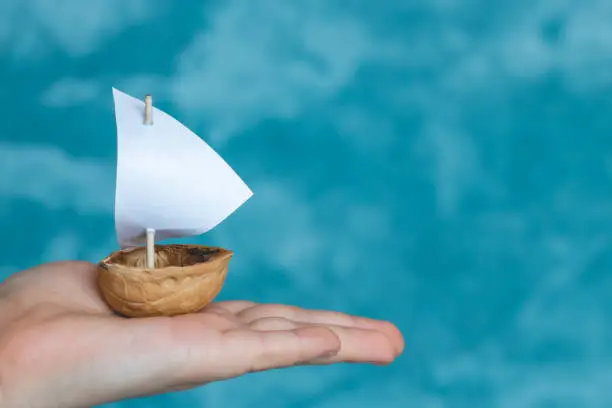 a small boat made of nutshell with a white sail in the palm of a child.