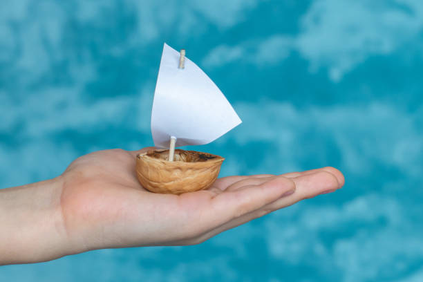 子供の手のひらに白い帆で一言でできている小さなボート。想像上の旅。 - ナッツの殻 ストックフォトと画像