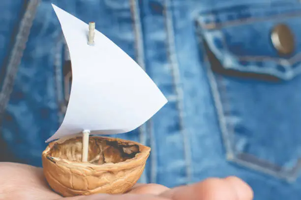 a small boat made of nutshell with a white sail in the palm of a child.