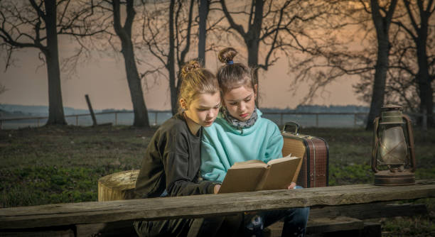 Girls read a book near an abandoned house. Girls read a book near the old manor on a wooden bench. Dystopian Romance Novels stock pictures, royalty-free photos & images