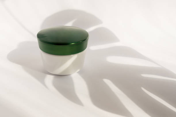 istock White blank mockup of bottle cream container with green cup. Monstera shadows. Professional tubes for facial and body treatment. 1215642243