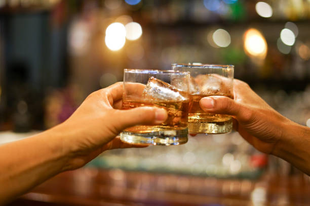 two men clinking glasses of whiskey drink alcohol beverage together at counter in the pub two men clinking glasses of whiskey drink alcohol beverage together at counter in the pub brandy photos stock pictures, royalty-free photos & images