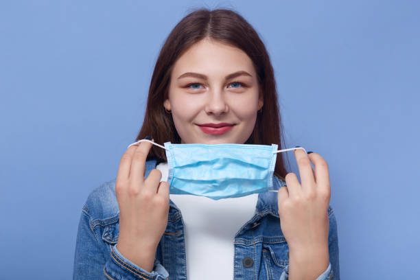 горизонтальный снимок красивой женщины надевает медицинскую маску, изолированную на синем фоне, девушка пытается избежать гриппа или коро - denim jacket стоковые фото и изображения