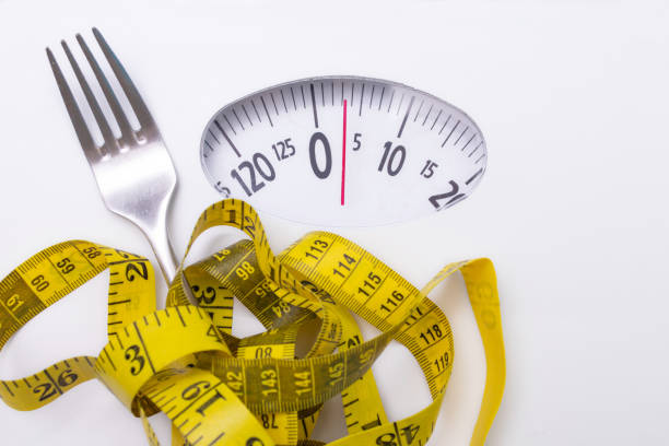 istock scale with measuring tape and fork, diet and weight loss concept 1215652259