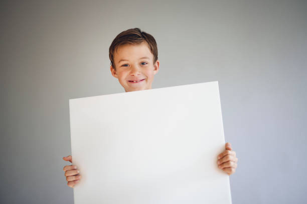 istock boy holding white sign in front of grey background 1215656466