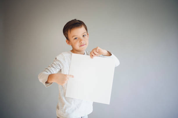 istock boy holding white sign in front of grey background 1215657070