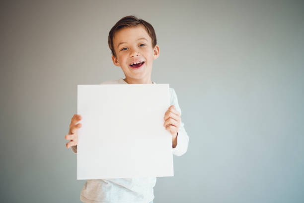 istock boy holding white sign in front of grey background 1215657080