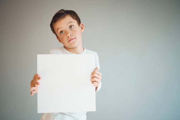 istock boy holding white sign in front of grey background 1215657122