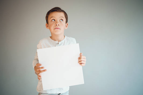 istock boy holding white sign in front of grey background 1215657242