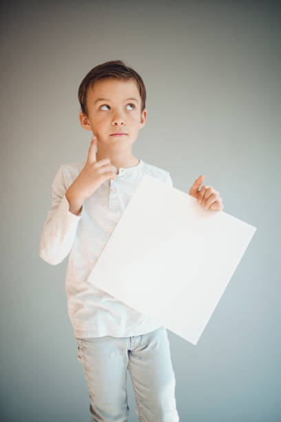 istock boy holding white sign in front of grey background 1215657354