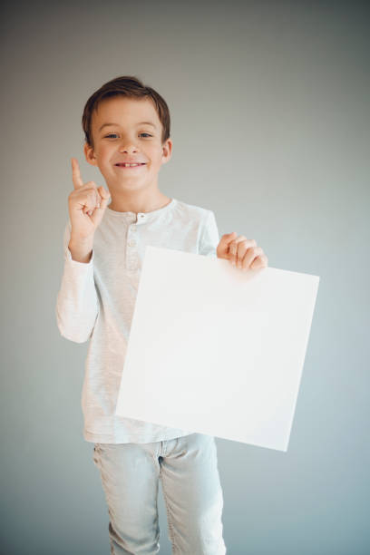 istock boy holding white sign in front of grey background 1215657431