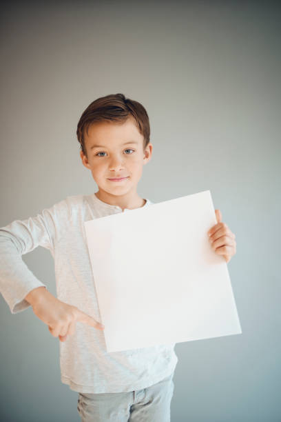 istock boy holding white sign in front of grey background 1215657705