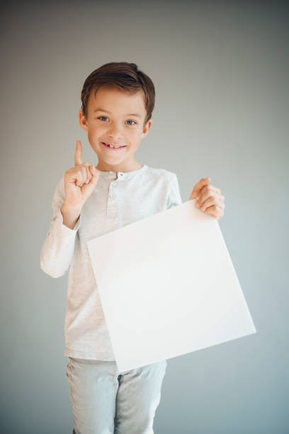 istock boy holding white sign in front of grey background 1215657891