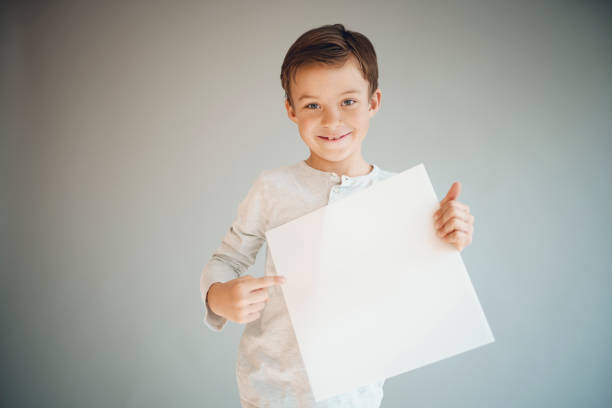 istock boy holding white sign in front of grey background 1215657984
