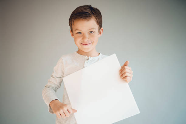istock boy holding white sign in front of grey background 1215657992