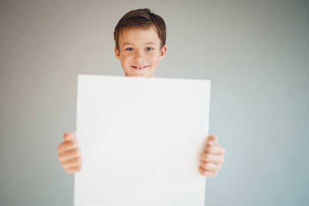 istock boy holding white sign in front of grey background 1215658009