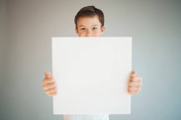 istock boy holding white sign in front of grey background 1215658059