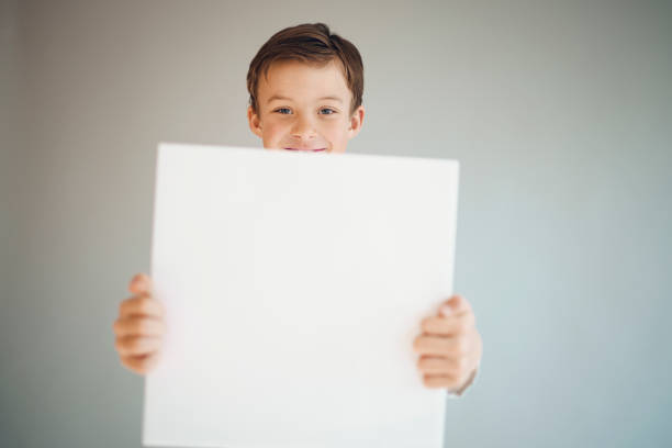 istock boy holding white sign in front of grey background 1215658071