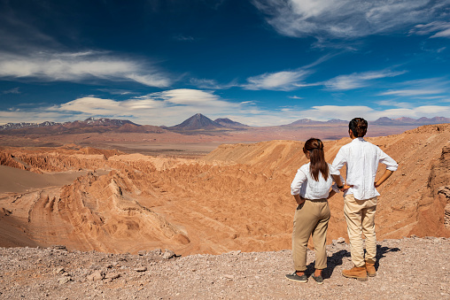 Two travellers with both hands on hips are looking at Mars Valley / Death Valley in Atacama Desert, Chile