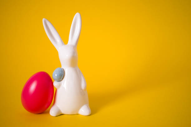 istock White porcelain Easter bunny with pink egg on yellow background 1215665097