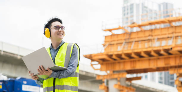 istock smart asian male professional civil engineer hand hold laptop site construction check with infastrcture and building background 1215665851