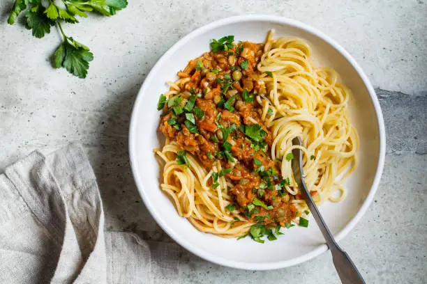 Photo of Vegetarian lentils bolognese pasta with parsley in white dish, top view. Healthy vegan food concept.