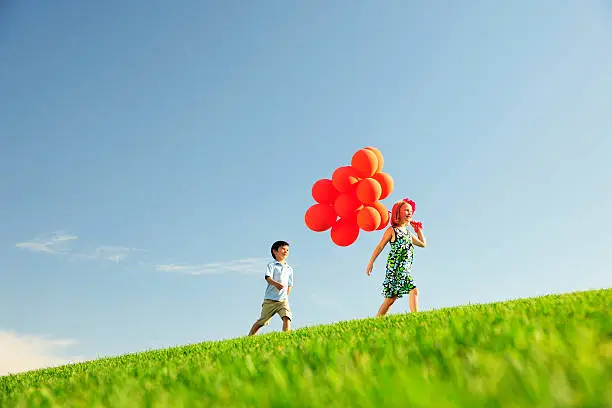 Photo of Two Friends Walking on a Hill with Red Balloons